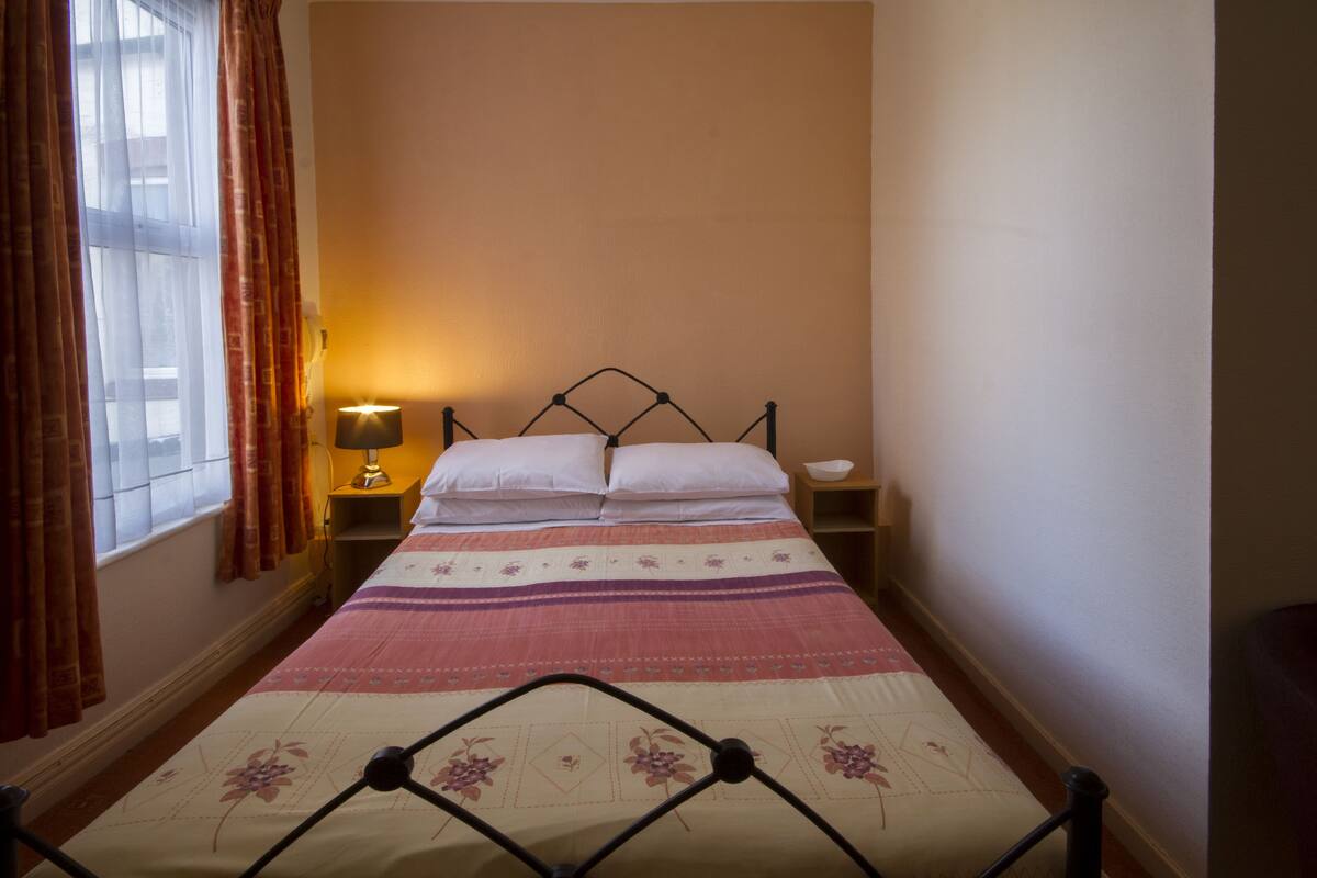 A single bed with a metal frame, a bedside table with a lamp, and a window with curtains.