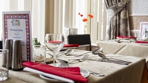 A dining table set with cutlery and a glass, a menu stand, and a vase with flowers. - Brooklands Over 50's Only (Blackpool)
