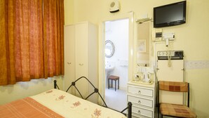 A bedroom with a bed, a dresser, a chair, a television, and a bathroom visible through an open door. - Brooklands Over 50's Only (Blackpool)