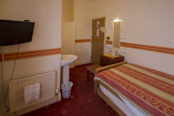 A small hotel room with a single bed, a bedside table, a mirror, a radiator, a sink, and a television mounted on the wall. - Brooklands Over 50's Only (Blackpool)
