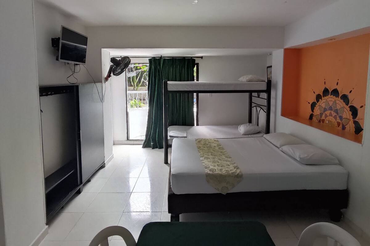 Une chambre avec un lit superposé, un bureau avec un ordinateur, un téléviseur fixé au mur et une fenêtre avec des rideaux.