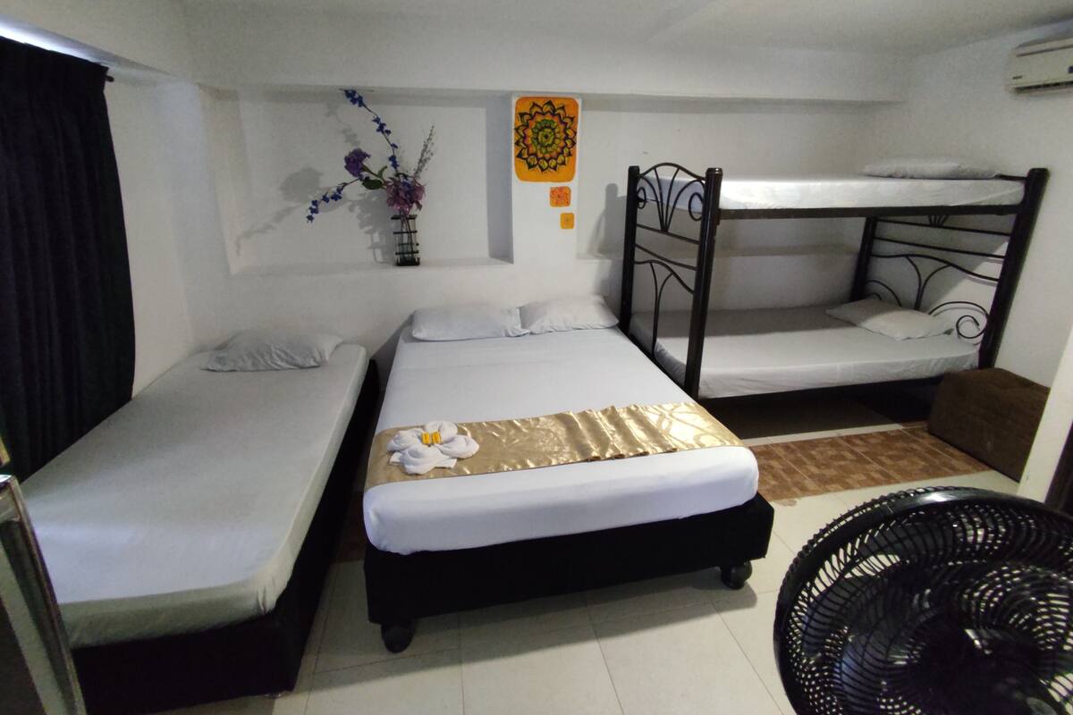 Une chambre avec deux lits simples, un lit superposé, une petite table, une chaise et un élément décoratif mural.