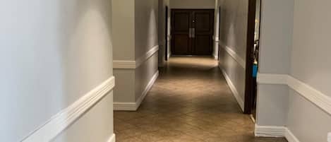 A corridor with beige tiled flooring, white walls, and a door at the end.