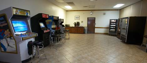 A room with arcade machines, a vending machine, and a refrigerator.