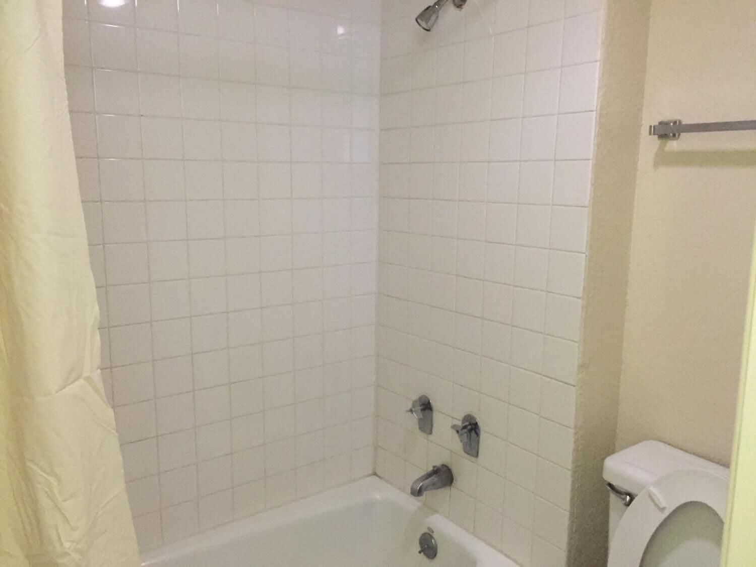 A bathroom with a white tiled shower, a bathtub, and a toilet.