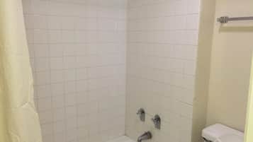 A bathroom with a white tiled shower, a bathtub, and a toilet.