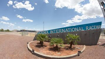 Une enseigne indiquant l’emplacement du circuit Phoenix International Raceway, avec un ciel dégagé et une zone de gravier bordée de palmiers.