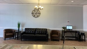 A lobby with a black leather sofa, two armchairs, a chandelier, a round wall clock, and a desk with a computer. - E-Z 8 Motel Phoenix Airporter (Phoenix)