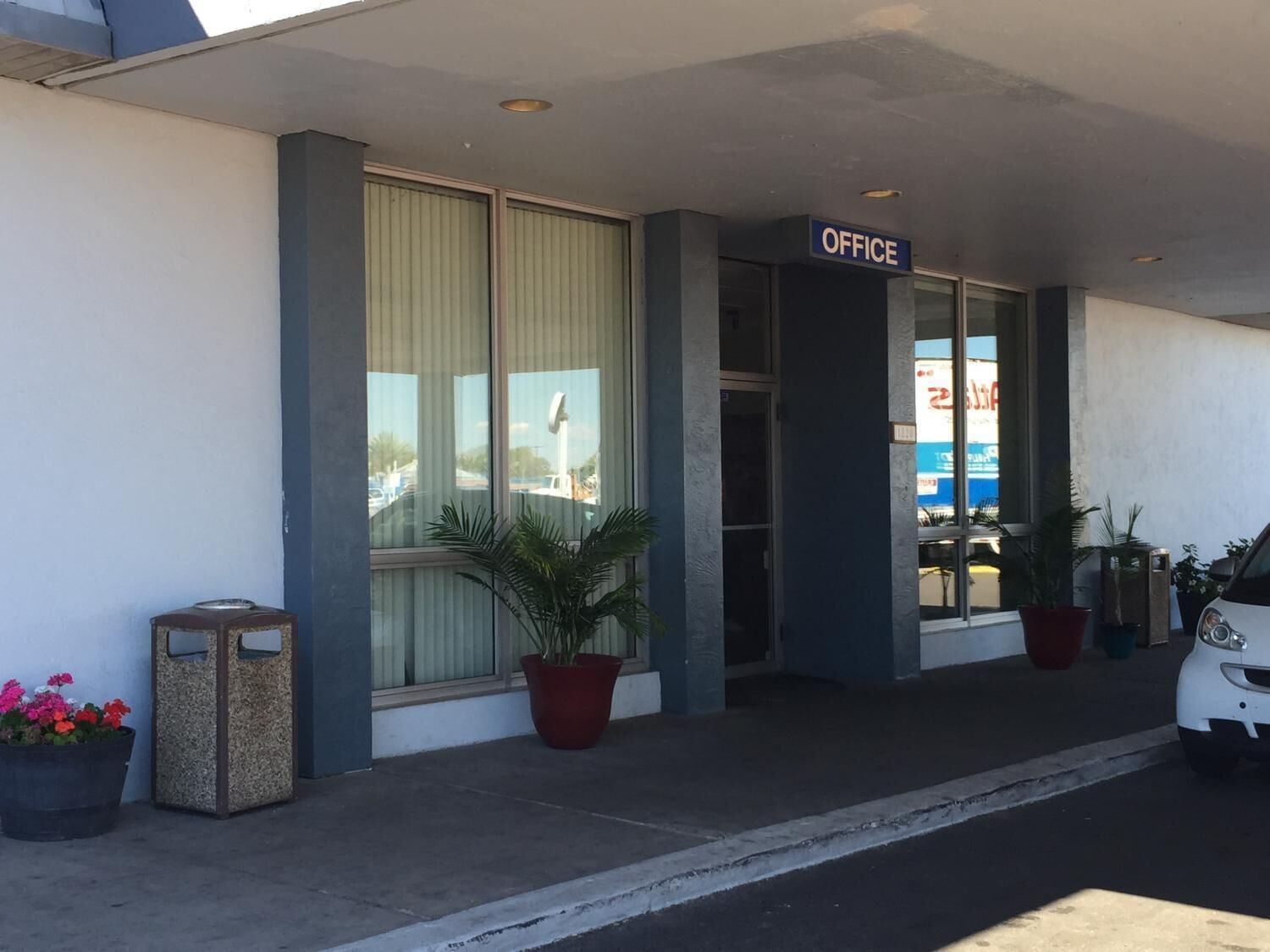 A building with a sign labeled "OFFICE" above the entrance. There are potted plants and a car parked outside.