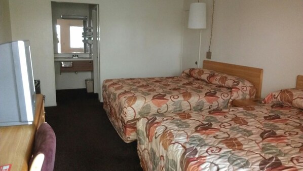 A hotel room with two beds, a desk, a mirror, and a small bathroom.