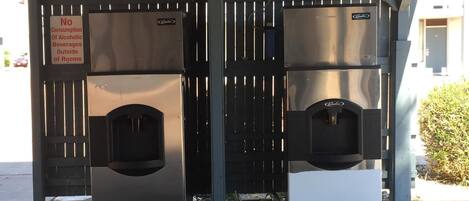 Casa de banho pública com aviso de proibição do consumo de álcool, duas pias e uma máquina de vendas automática.