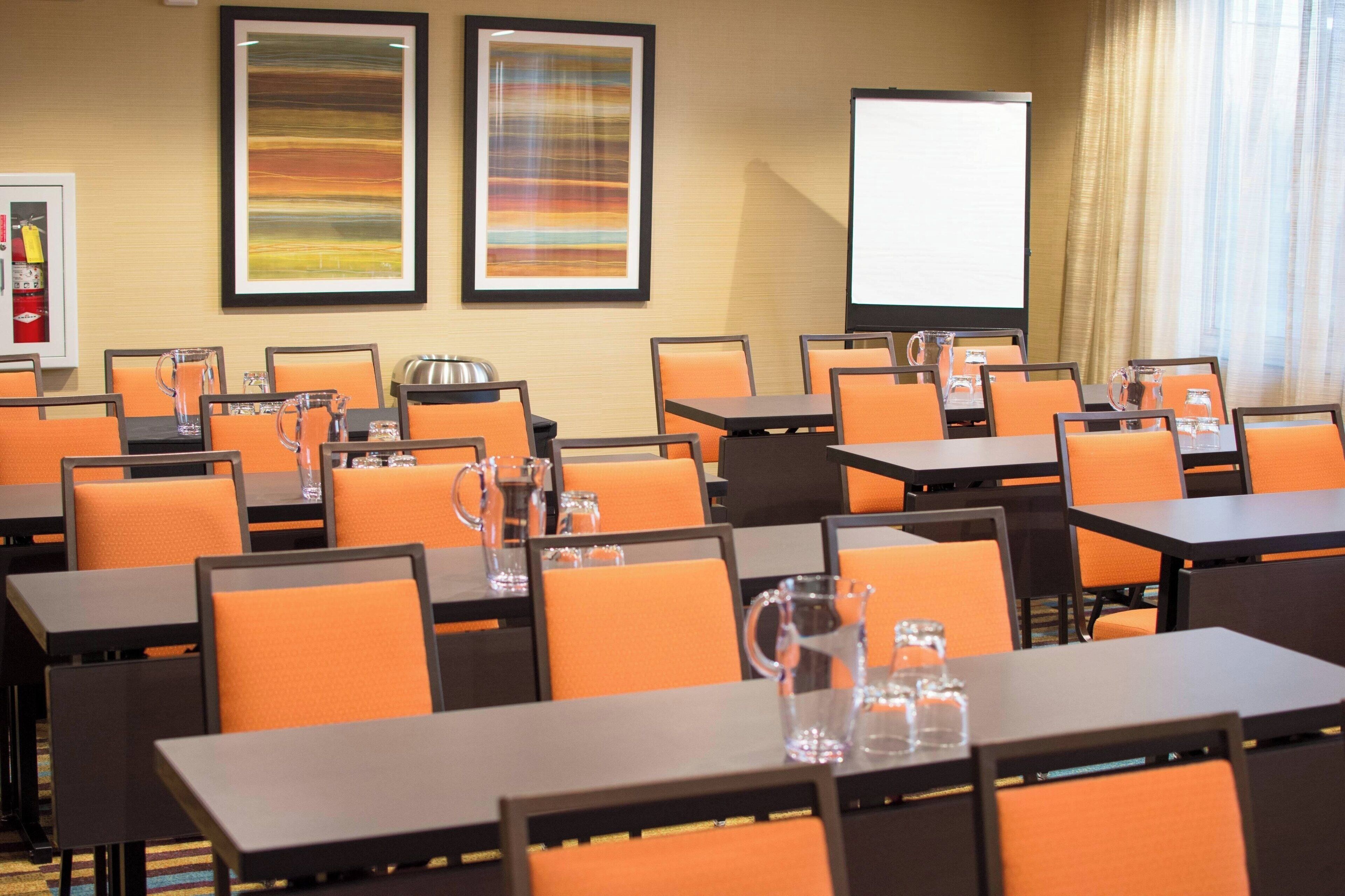 A conference room with tables and chairs, a projector screen, and framed artwork on the walls.
