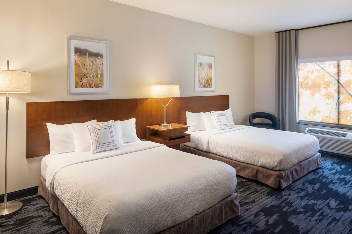 A hotel room with two beds, a wooden headboard, a floor lamp, and artwork on the walls.