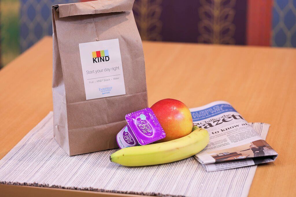 A KIND bag with a label, an apple, a banana, and two purple packages on a newspaper.