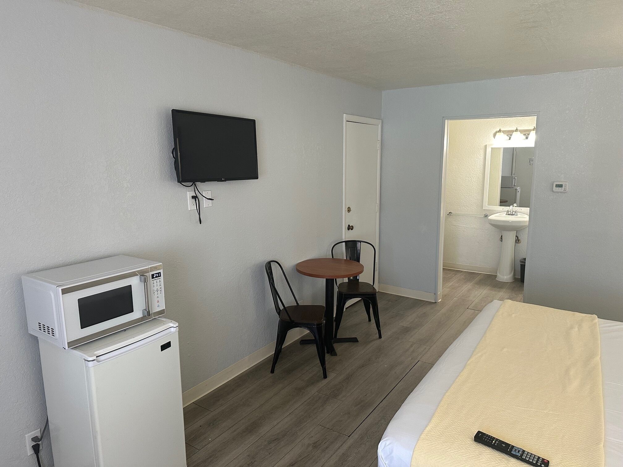 A hotel room with a bed, a microwave, a TV, a small table with a chair, and a bathroom visible through an open door.