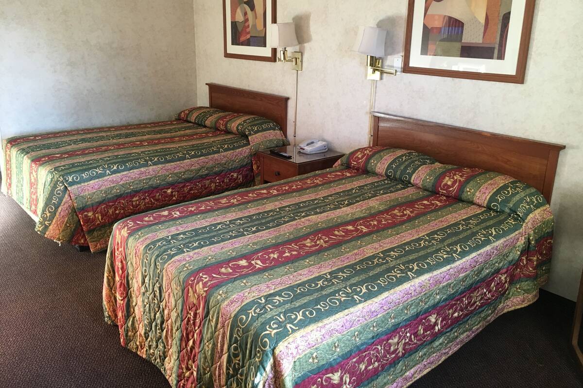 A hotel room with two single beds, a nightstand, a lamp, and two framed pictures on the wall.