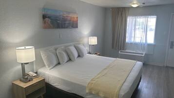 Ein Hotelzimmer mit einem großen Bett, zwei Nachttischlampen, einem Gemälde an der Wand, einem Fenster mit Vorhängen und einer Deckenleuchte.