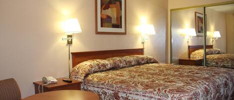 A hotel room with a bed, a round table, two lamps, a phone, and a painting on the wall.