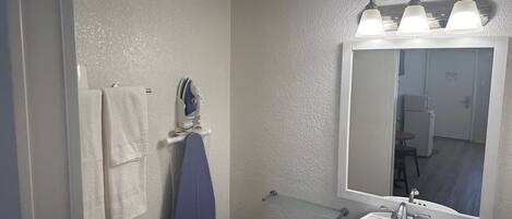 A bathroom with a white sink, a mirror with three lights, a towel rack, and a shower area.