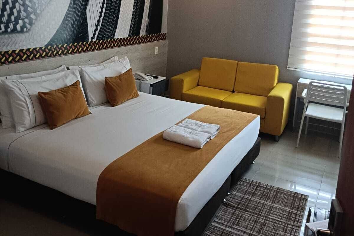 A hotel room with a large bed, a yellow armchair, a small table, and a patterned wall.