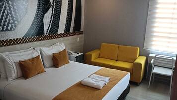 A hotel room with a large bed, a yellow armchair, a small table, and a patterned wall.