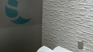 Un baño con pared de textura de piedra, un logotipo a la izquierda y un perchero con toallas.