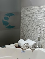 Un baño con pared de textura de piedra, un logotipo a la izquierda y un perchero con toallas.
