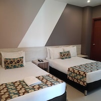 Habitación de hotel con dos camas, cada una con una colcha estampada, una mesita de noche con teléfono, y una puerta a la derecha.