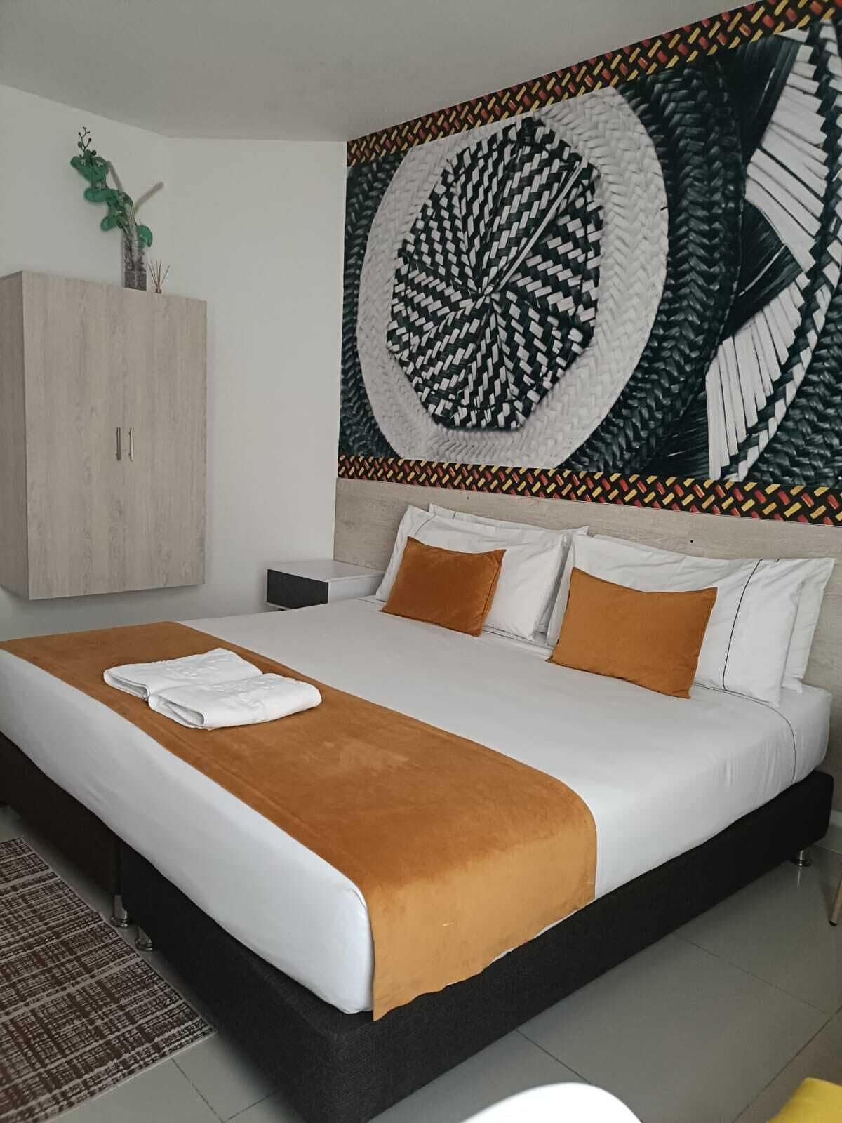 A modern hotel room with a large bed, a wooden wardrobe, and a decorative wall piece.