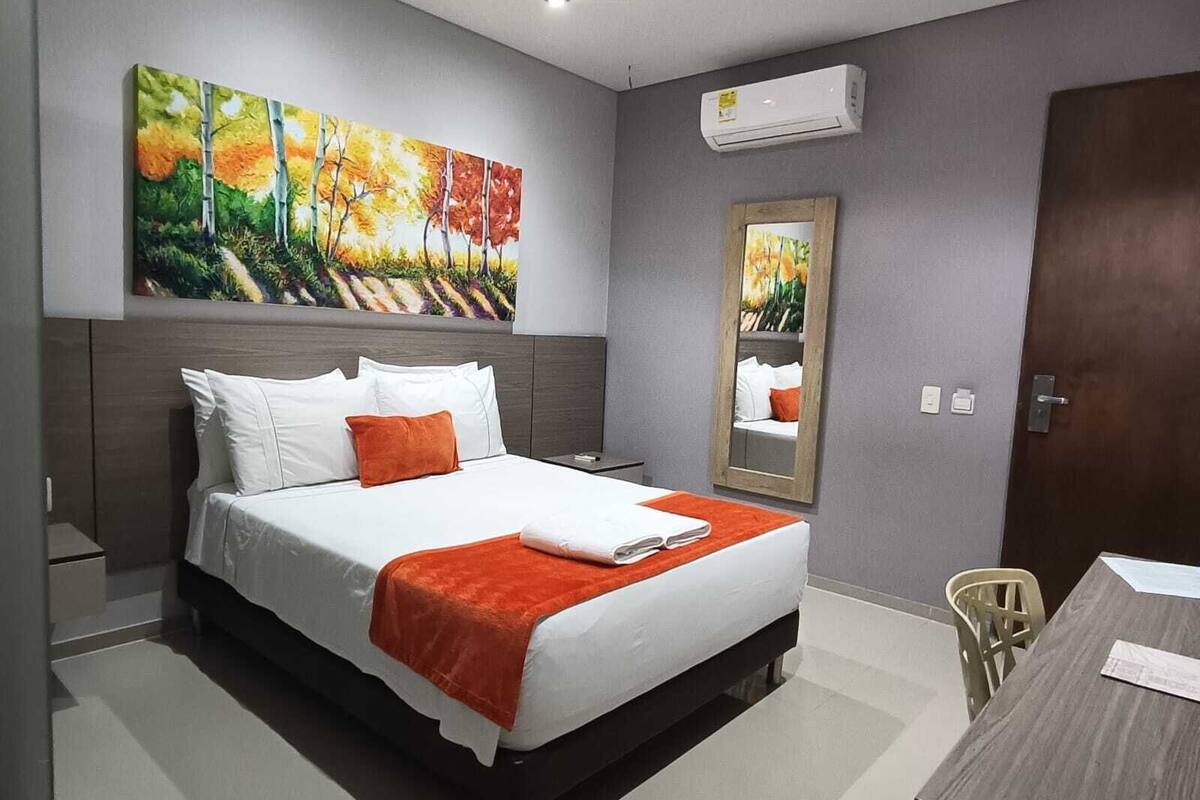 A modern hotel room with a large bed, a desk, and a painting on the wall.