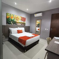 A modern hotel room with a large bed, a desk, and a painting on the wall.