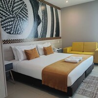 Una habitación de hotel con una cama, un sillón amarillo y una gran obra de arte abstracta en la pared.