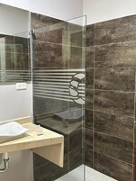 Un baño con cabina de ducha de vidrio, un lavamanos con encimera de mármol y baldosas oscuras con diseño.