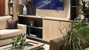 A modern hotel lobby with a large flat-screen TV displaying the Santa Clara Boutique logo. There is a sofa, a coffee table with magazines, and a potted plant. - Hotel Santa Clara Boutique (Montería)