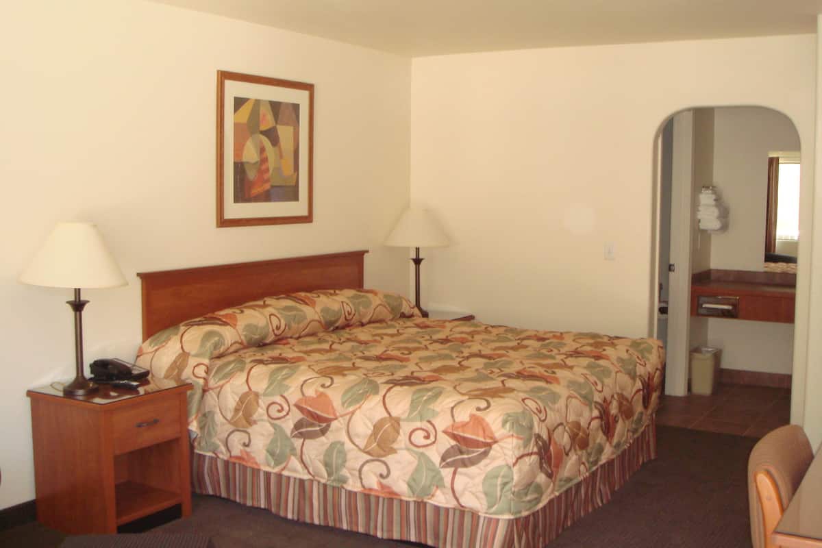Una habitación de hotel con una cama grande, dos lámparas de noche, una mesita de noche, una silla, un escritorio y un espejo.