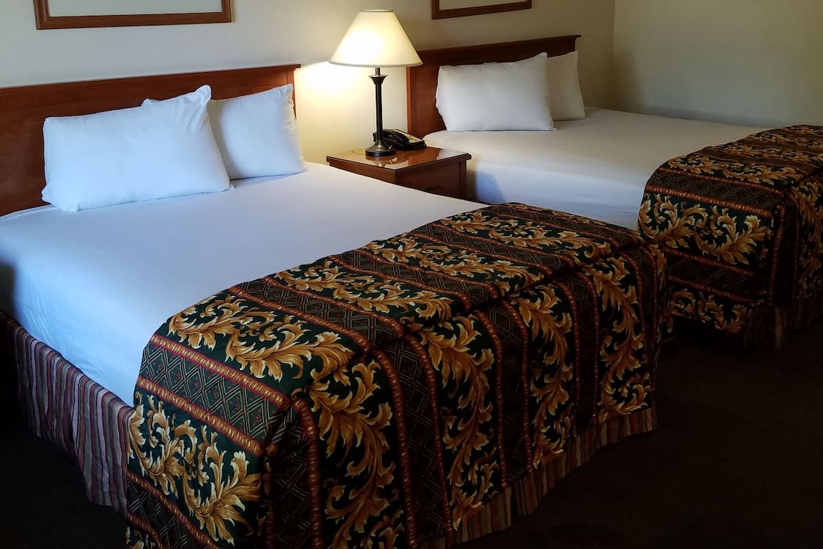 Una habitación de hotel con dos camas, una mesita de noche con lámpara y dos cuadros enmarcados en la pared.