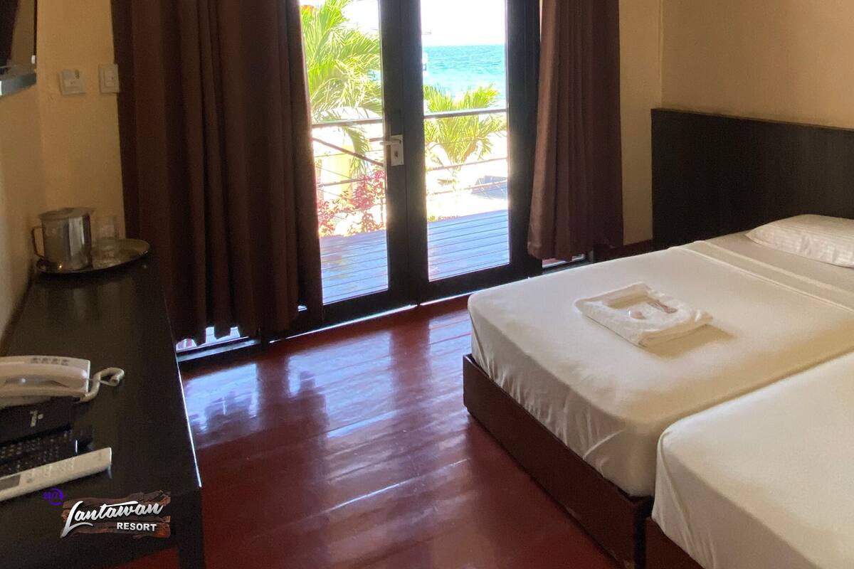 A hotel room with two beds, a desk with a phone, and a view of the ocean through a sliding door.