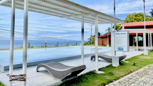 A pool area with a view of the ocean, covered seating, and a sign indicating pool rules. - 24/7 Lantawan Resort (Oslob)