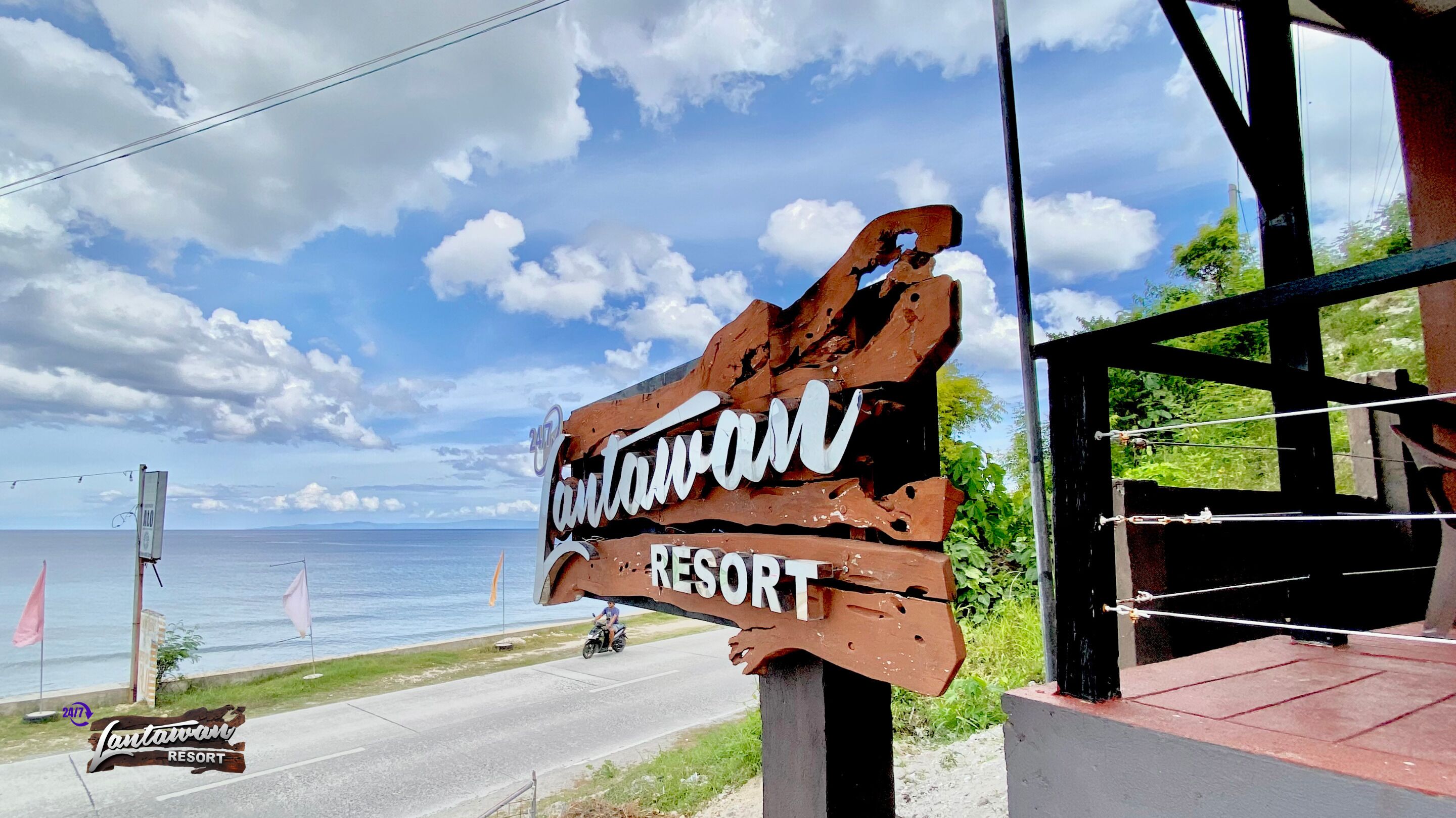 A rustic sign for 'Tavanan Resort' with a view of the sea and a clear sky.
