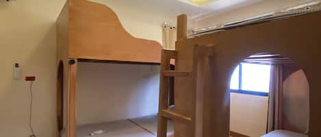A bunk bed room with a ladder, a window, and a power outlet on the wall.