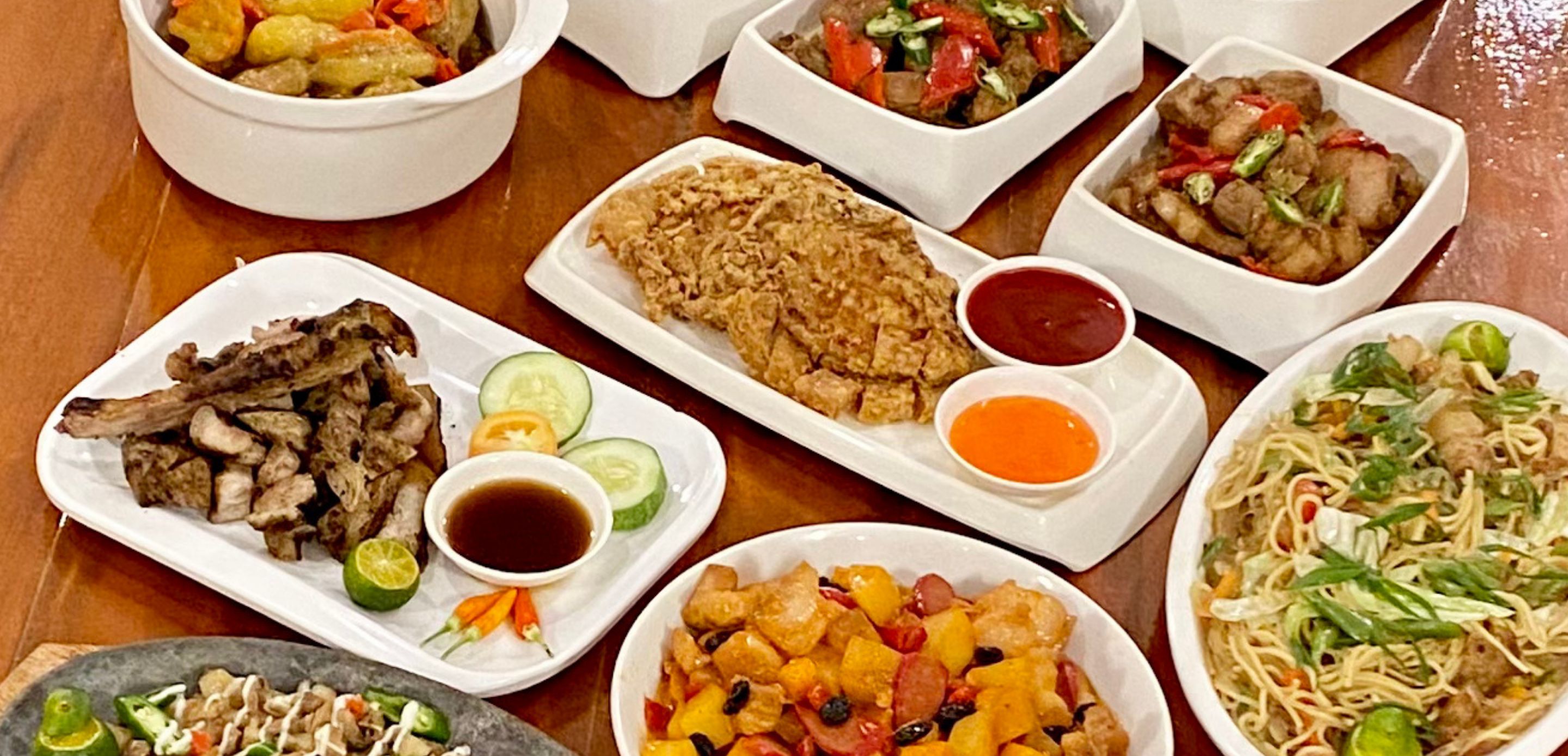 A variety of dishes including grilled meat, fried items, and noodles, served on white plates with condiments.