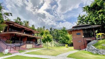 A resort with a two-story building, a thatched-roof structure, and a paved pathway.