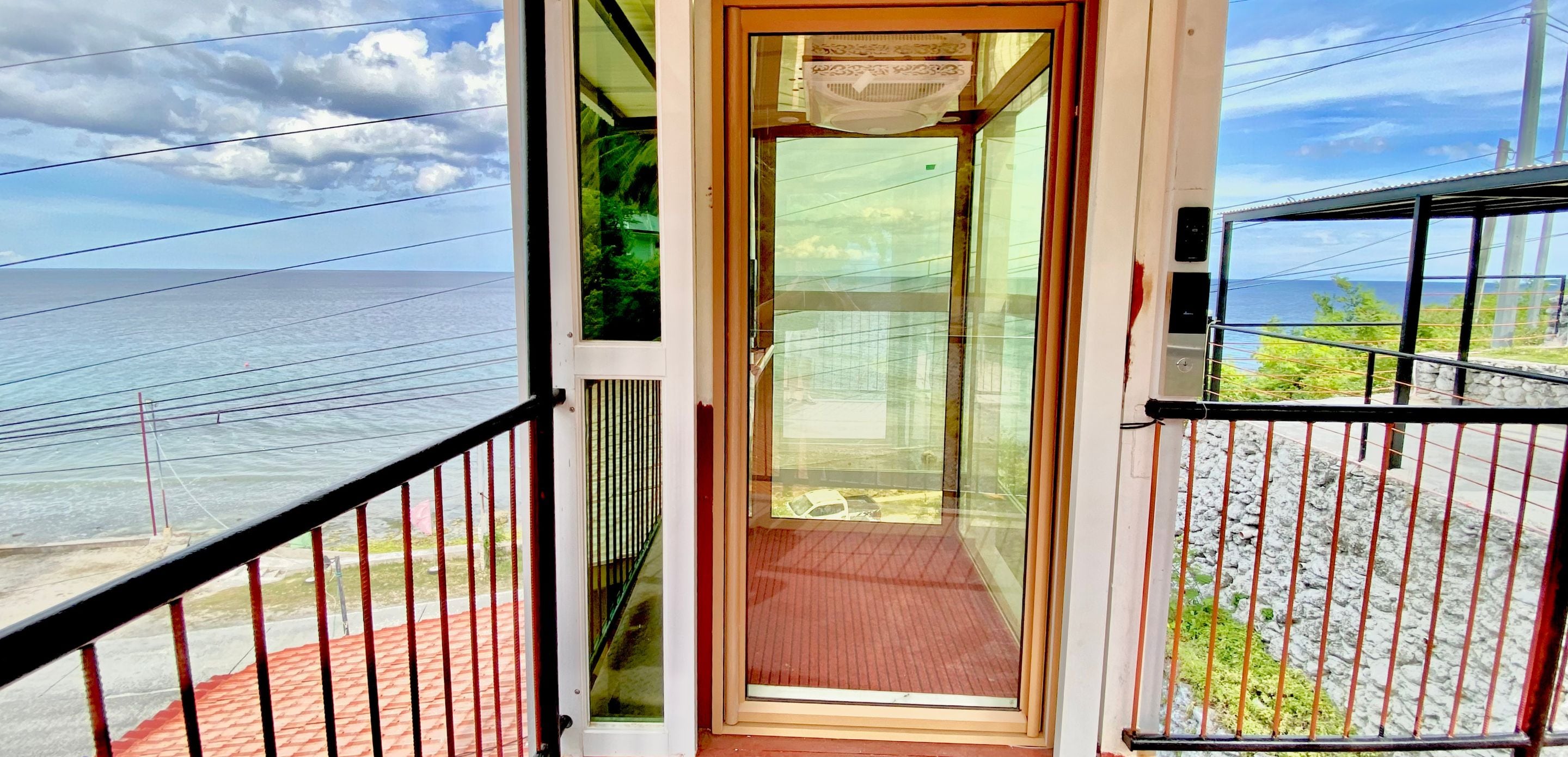 Een balkon met een glazen deur naar een kamer, met uitzicht op een strand en de oceaan.
