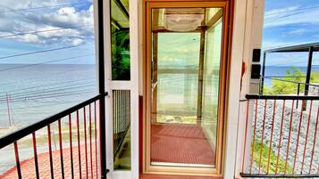 Een balkon met een glazen deur naar een kamer, met uitzicht op een strand en de oceaan.