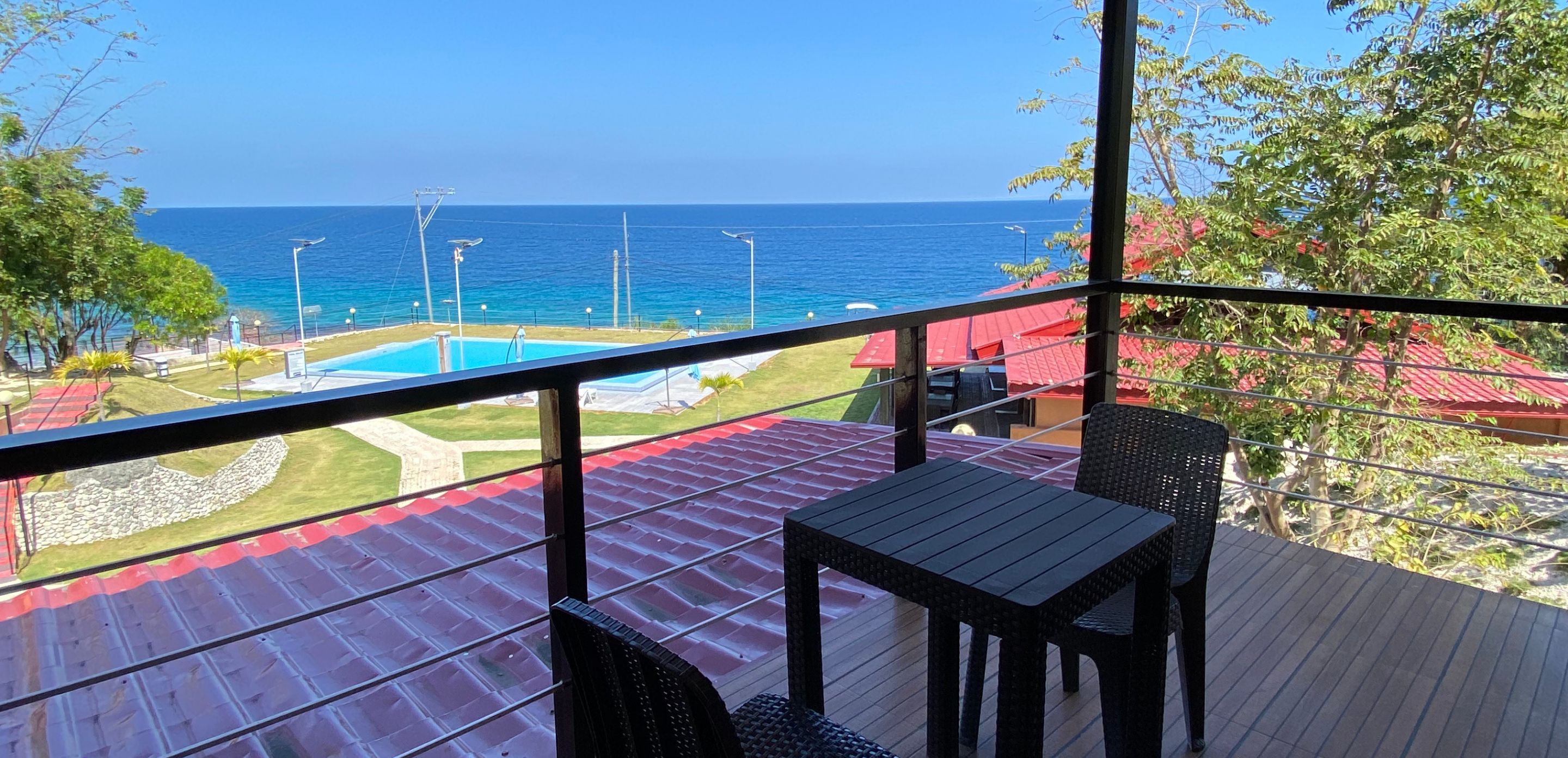A deck with a table and chairs overlooking a pool and the ocean.