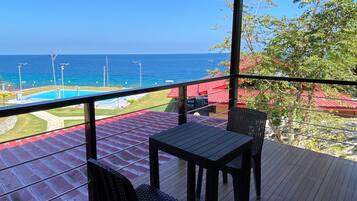 A deck with a table and chairs overlooking a pool and the ocean.