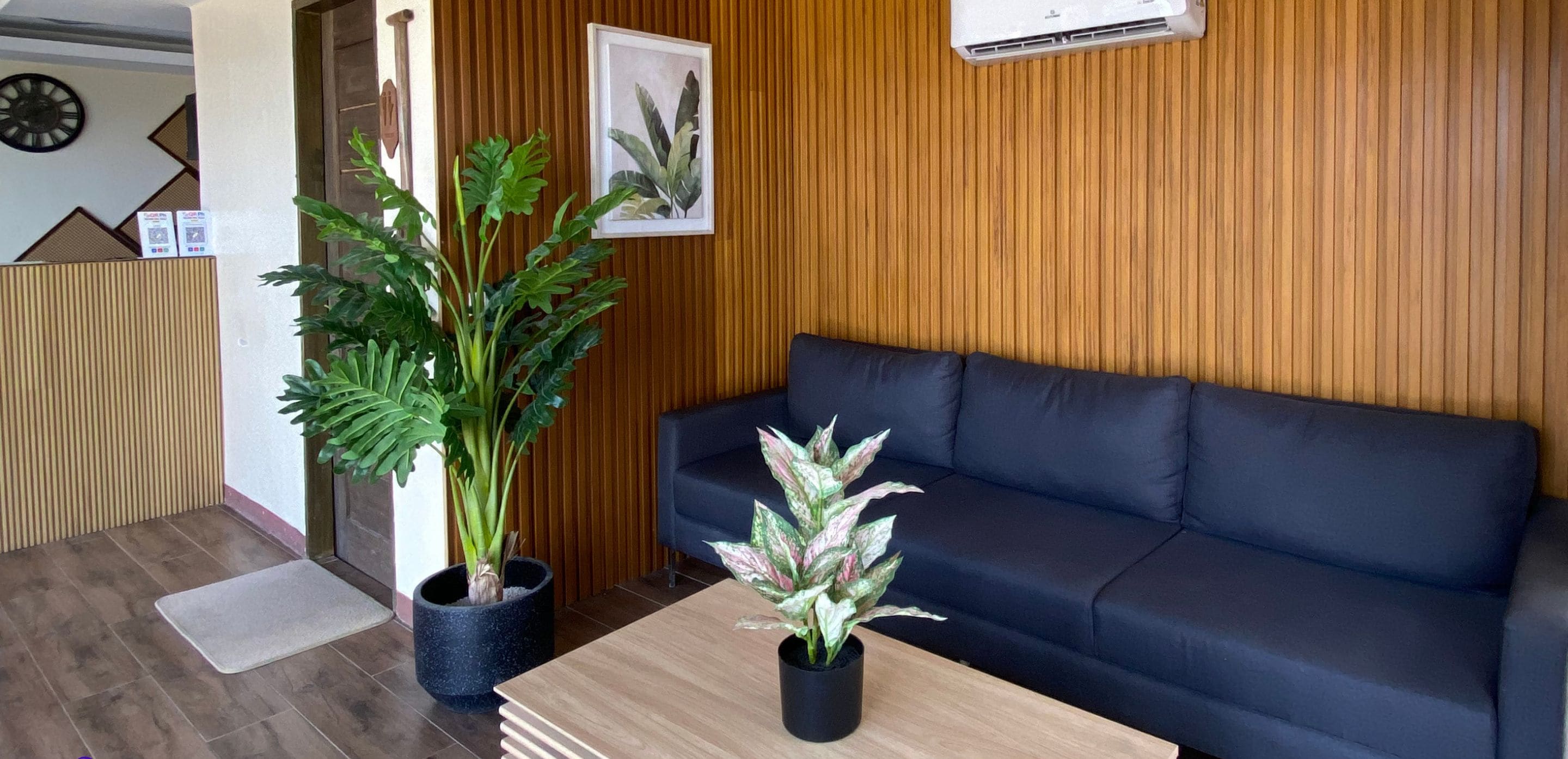 A modern living room with a dark blue sofa, wooden panel walls, and two potted plants.