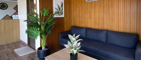 Un salón moderno con un sofá azul oscuro, paneles de madera y dos plantas en macetas.