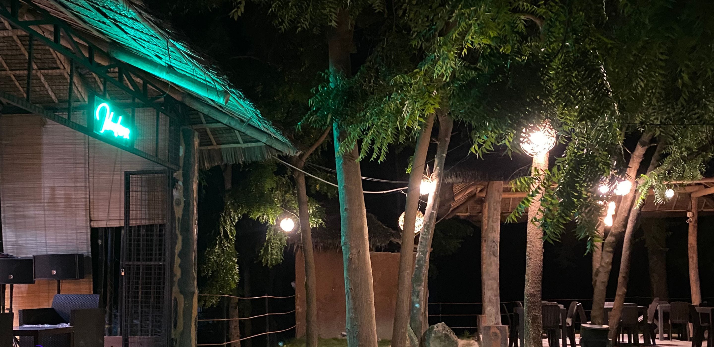 Resort com edifício iluminado, área externa para sentar e árvores.