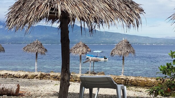 Een strand met rieten parasols, een bank en een rotsachtige kustlijn.